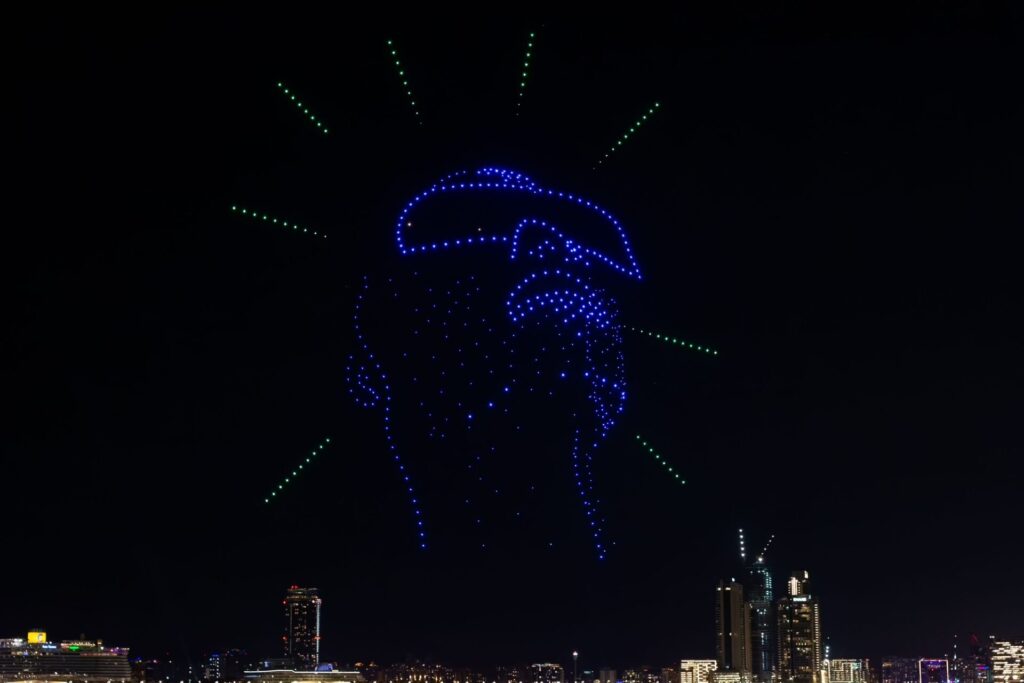 Illuminated blue drones glowing in the black night sky and forming a face with sunglasses